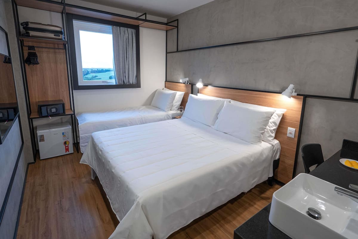 Quarto de hotel com duas camas, uma kitchenette pequena, janela com cortinas e vista para o exterior.