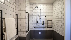 A modern bathroom with white and black tiled walls, a black towel rack, a shower with a handheld showerhead, and a small shelf. - Ibis Guarapuava (Guarapuava)