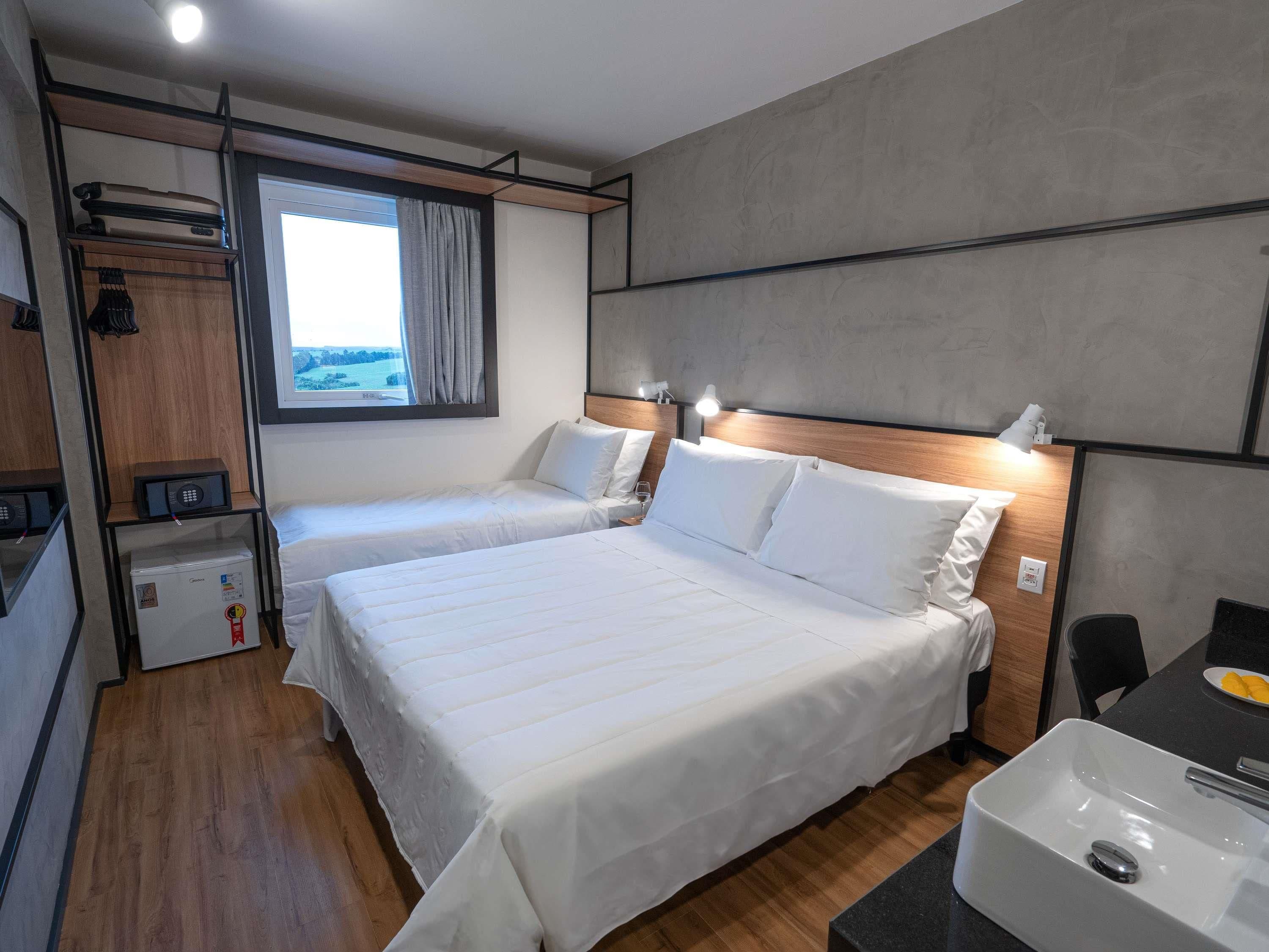 Habitación de hotel con dos camas, una kitchenette pequeña, una ventana con cortinas y vistas al exterior.