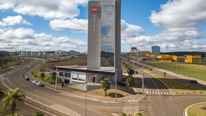 Un hotel moderno con un letrero vertical llamativo, ubicado cerca de una autopista con varios carriles y un paso de peatones.