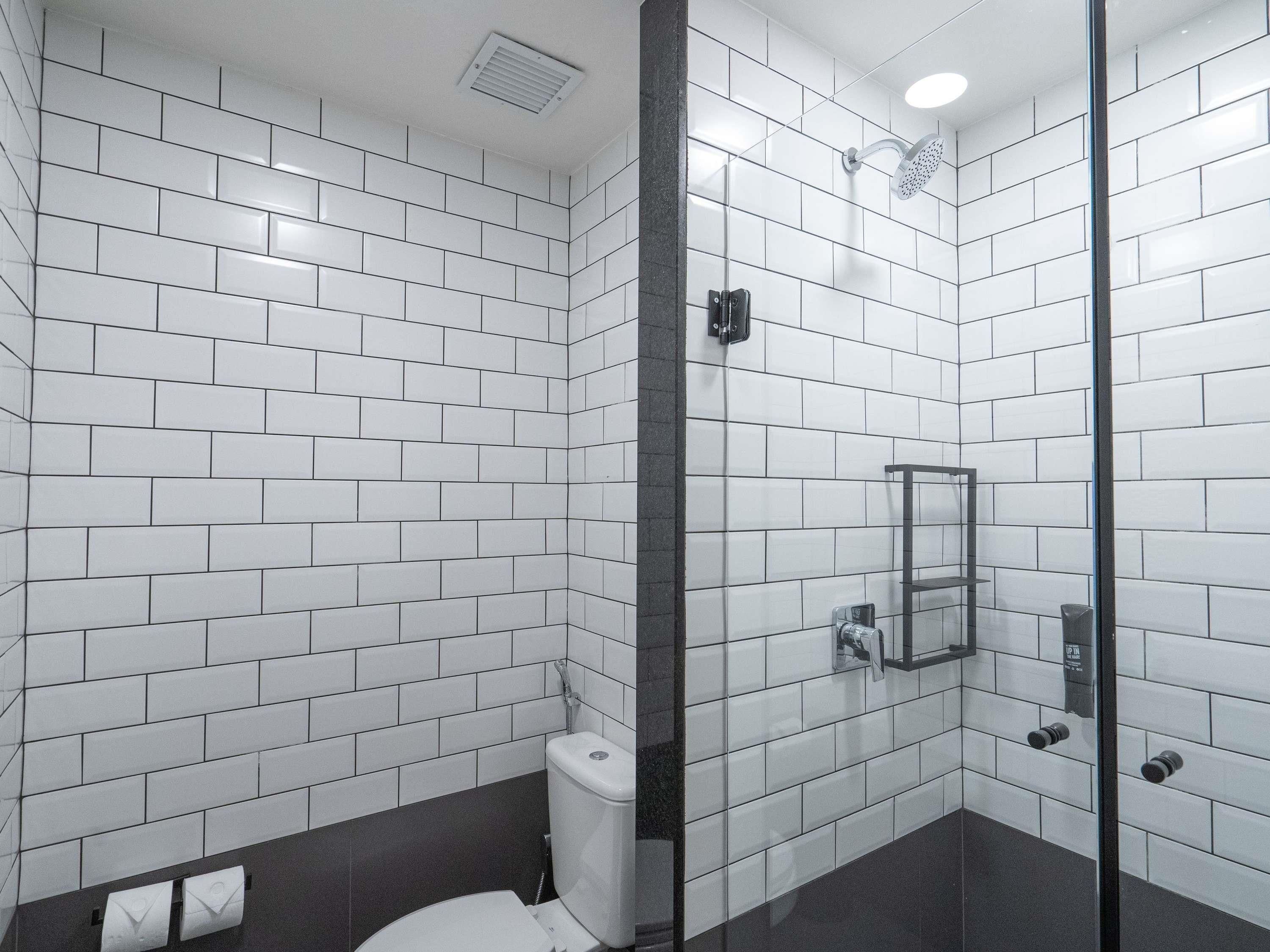 A modern bathroom with white subway tiles, a glass shower enclosure, and a toilet with a dark floor.