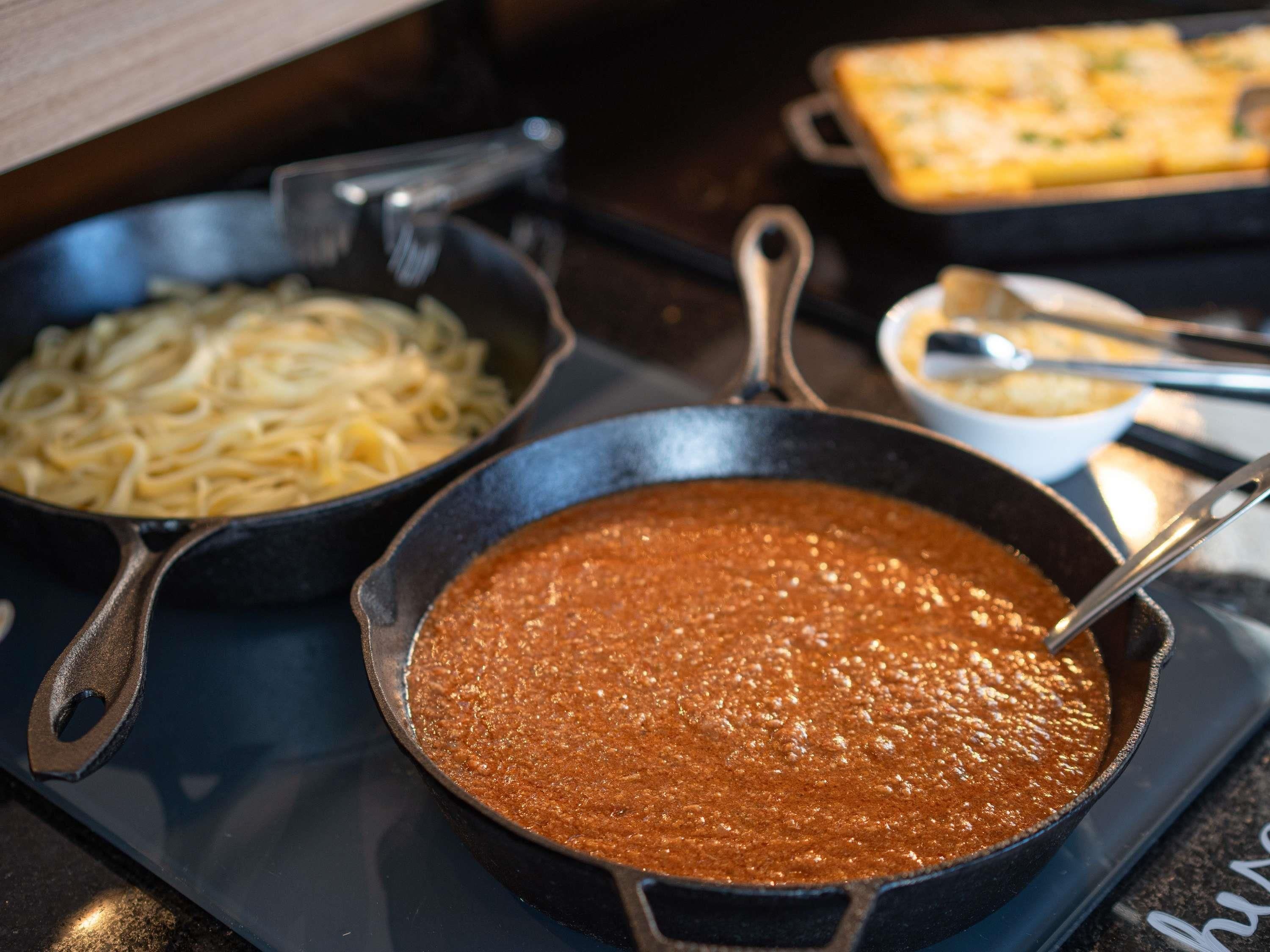 A pan of red sauce, a pan of noodles, and a baking dish on a stovetop.