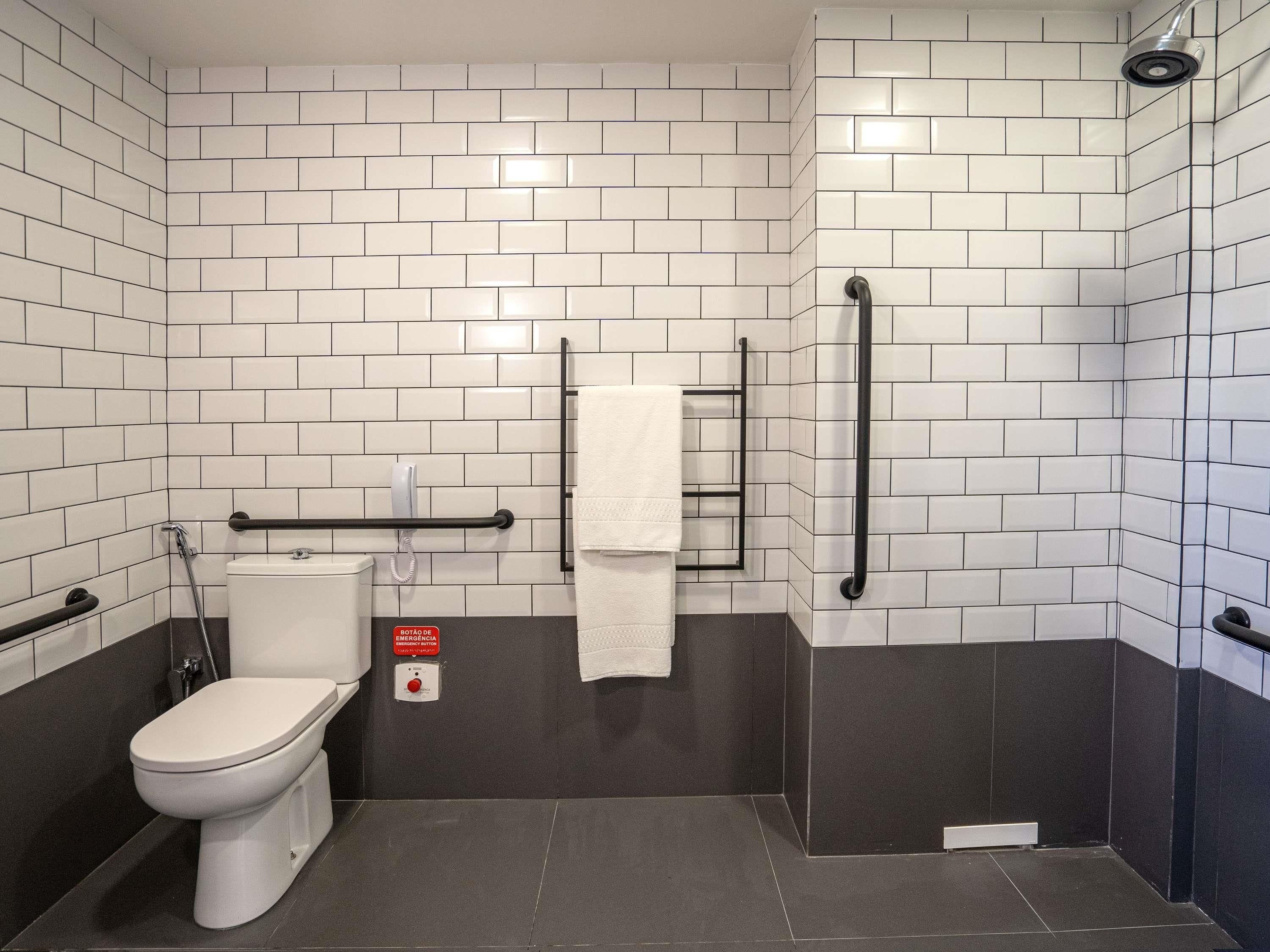 A bathroom with white subway tiles, a toilet, a shower, and a handrail.
