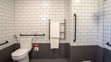 A bathroom with white subway tiles, a toilet, a shower, and a handrail.
