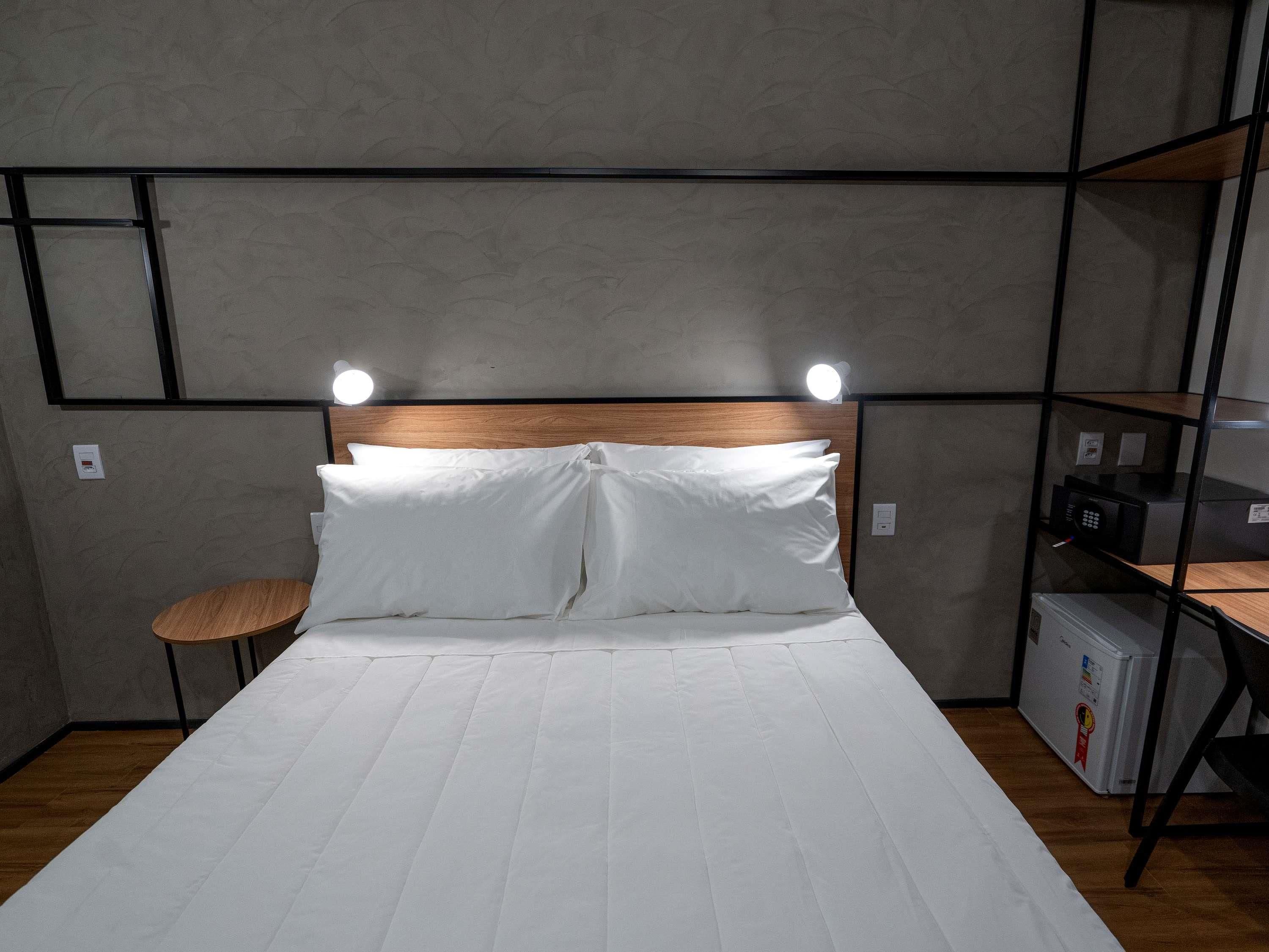 Una cama bien hecha con sábanas blancas, un cabecero de madera y dos lámparas de noche.