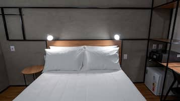 Una cama bien hecha con sábanas blancas, un cabecero de madera y dos lámparas de noche.