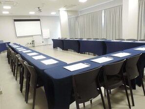 A conference room with long tables, chairs, a projector screen, and a whiteboard. - Ibis Guarapuava (Guarapuava)