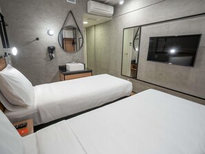 A hotel room with two beds, a bedside table with a white sink, a mirror, and a TV.