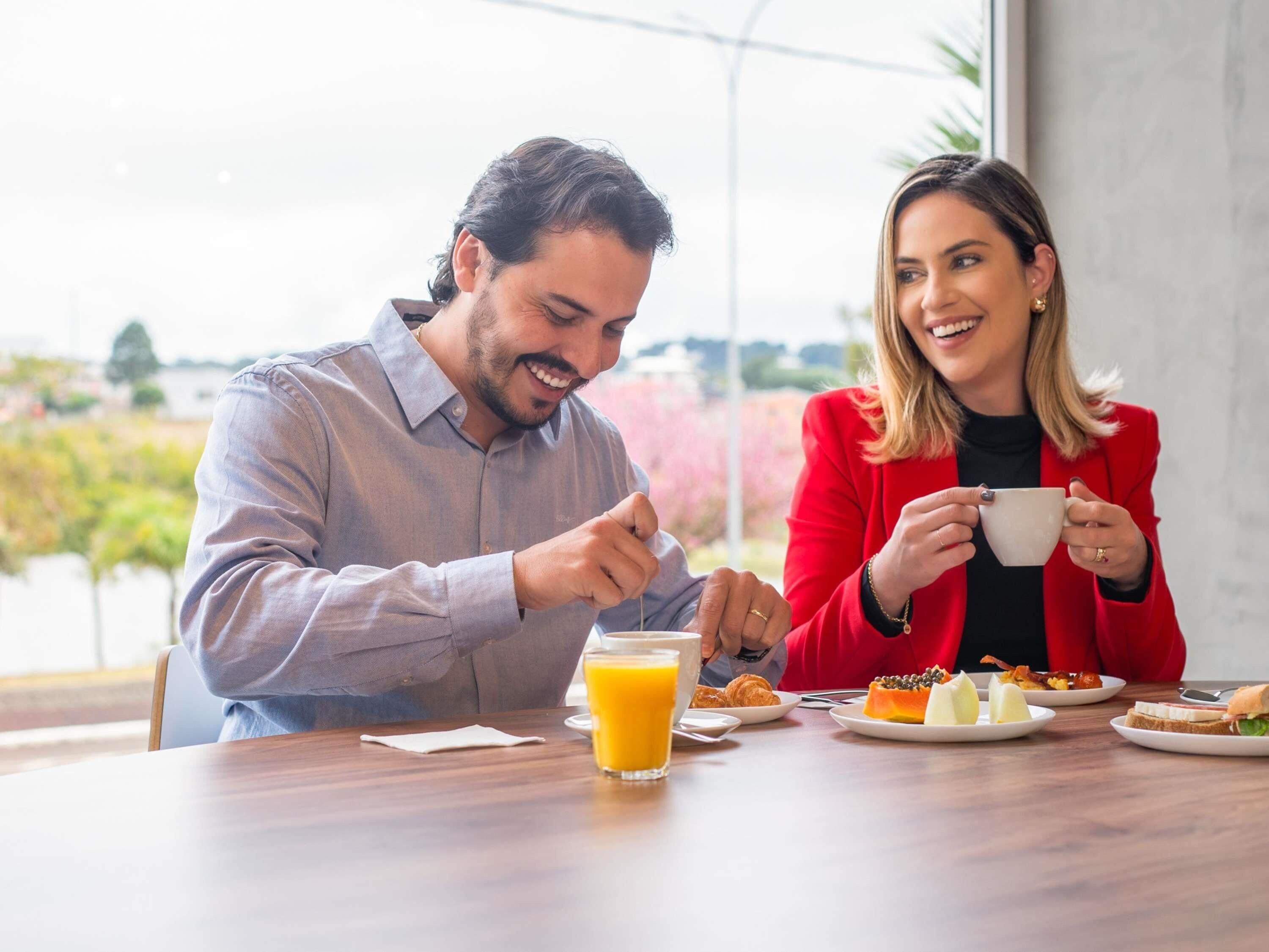 A dining table with breakfast items, a glass of orange juice, and a view of greenery outside.