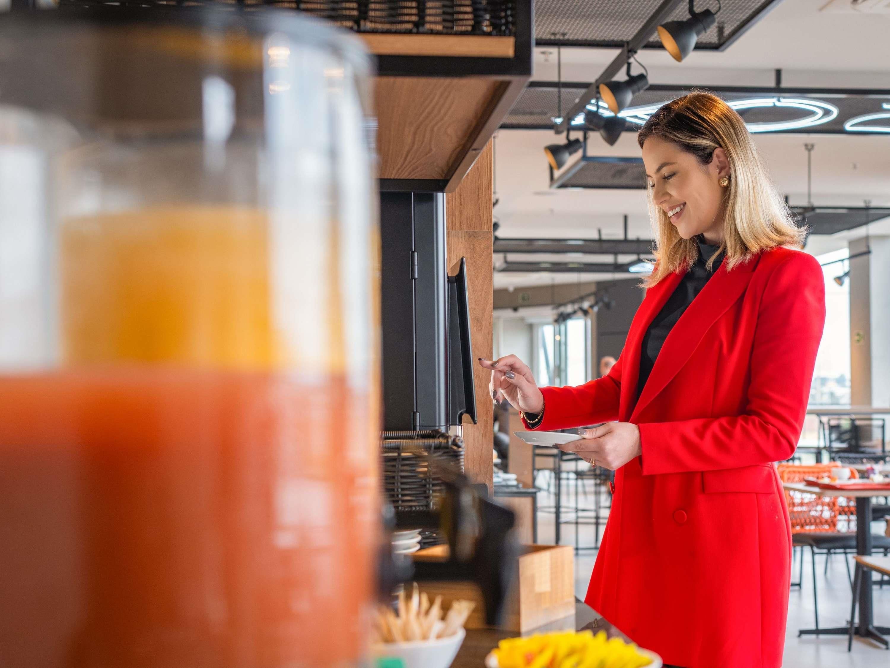 A person in a red coat standing at a counter with a glass container and a bowl of fries.