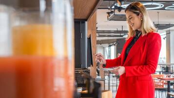 A person in a red coat standing at a counter with a glass container and a bowl of fries.