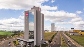 A modern hotel with a prominent glass facade, a rooftop terrace, and a view of a highway and surrounding landscape. - Ibis Guarapuava (Guarapuava)