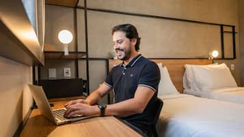 A man working at a laptop in a hotel room with a bed and a desk.