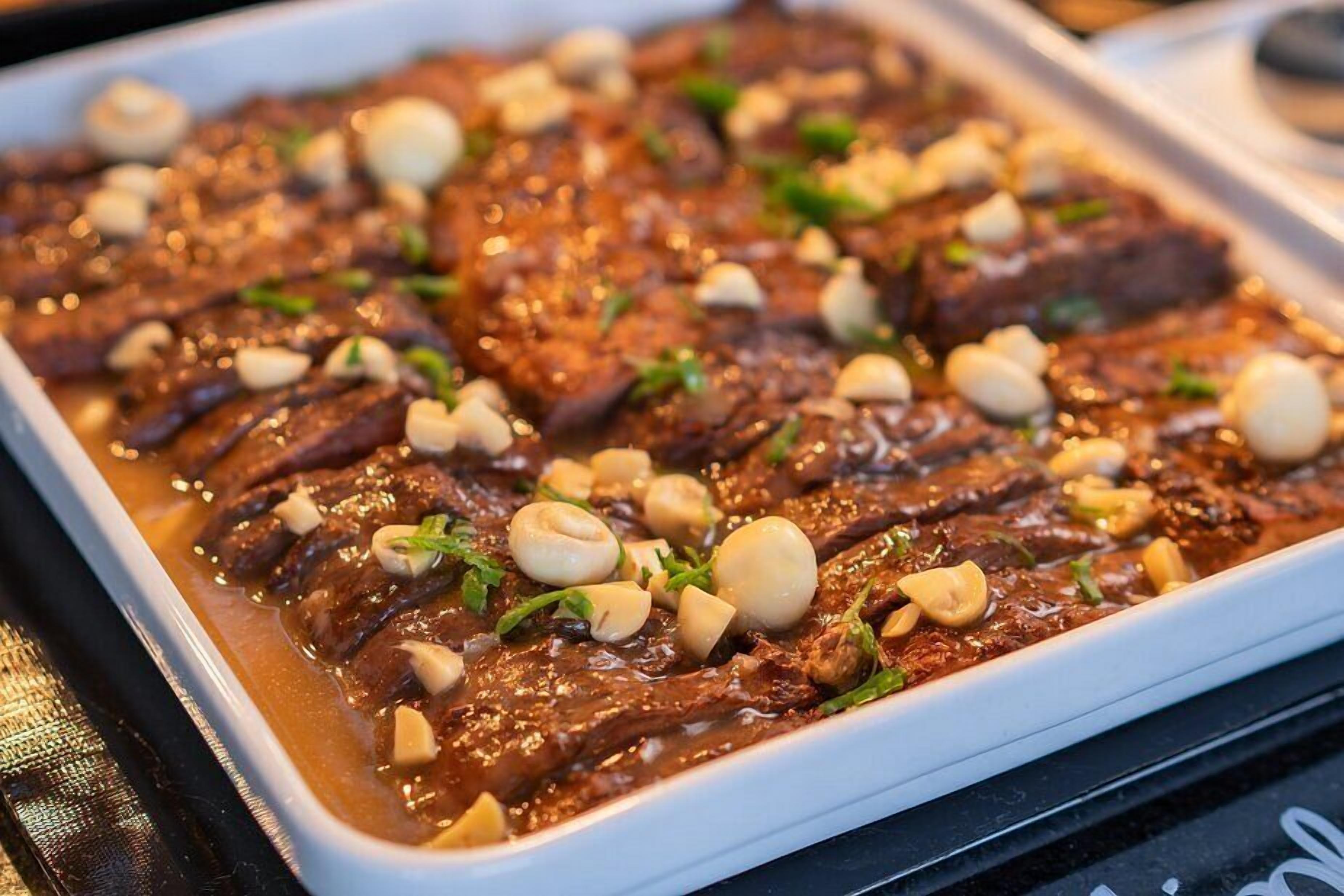 A dish of sliced meat with a rich sauce, garnished with nuts and herbs.