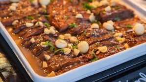 A dish of sliced meat with a rich sauce, garnished with nuts and herbs. - Ibis Guarapuava (Guarapuava)