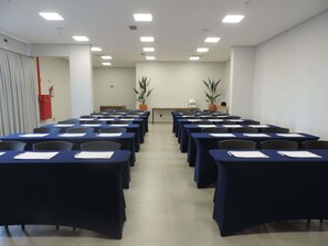 A conference room with rows of tables and chairs, a fire extinguisher, and two potted plants.