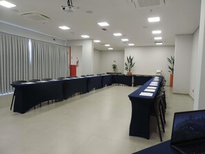 A conference room with a long table, chairs, a projector, and potted plants.