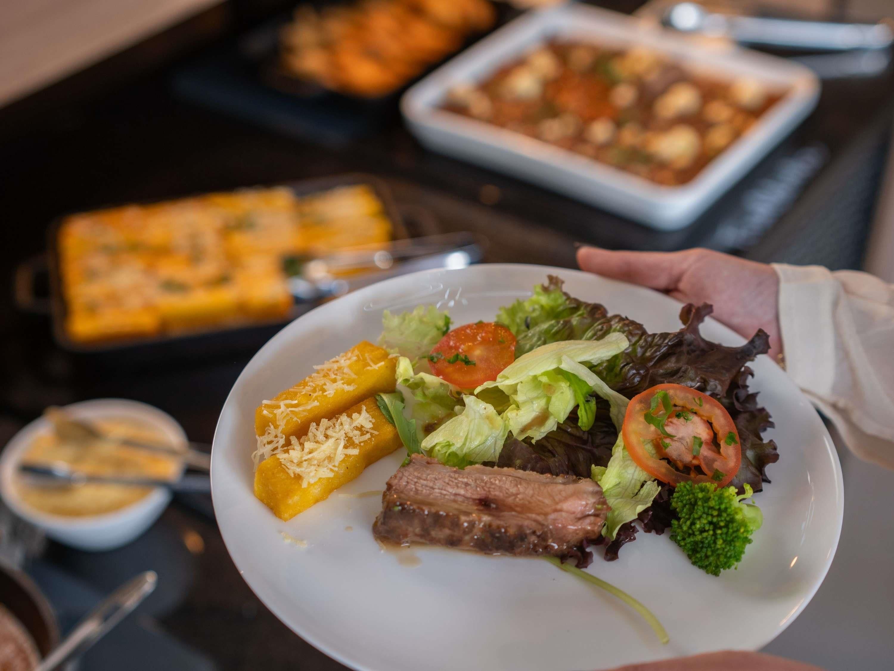 A person holding a plate with a salad, steak, and a side dish.