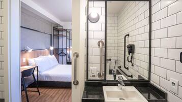 A hotel room with a bed, bedside table, lamp, and a bathroom with a sink, mirror, and towel rack.