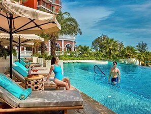 A poolside area with lounge chairs, a table with a bottle and glass, and a building with a dome in the background.