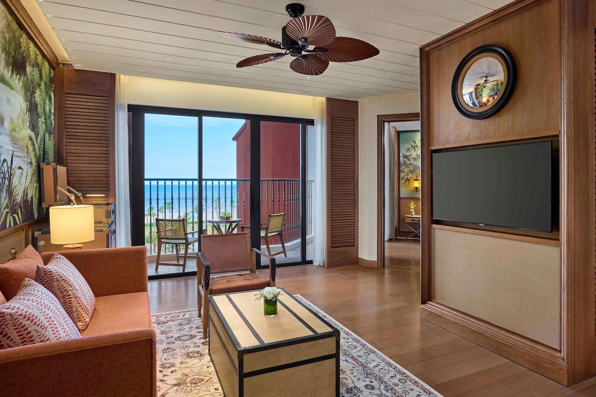 Un salón amplio con sofá, mesa de centro y televisor. Balcón con vista al océano.