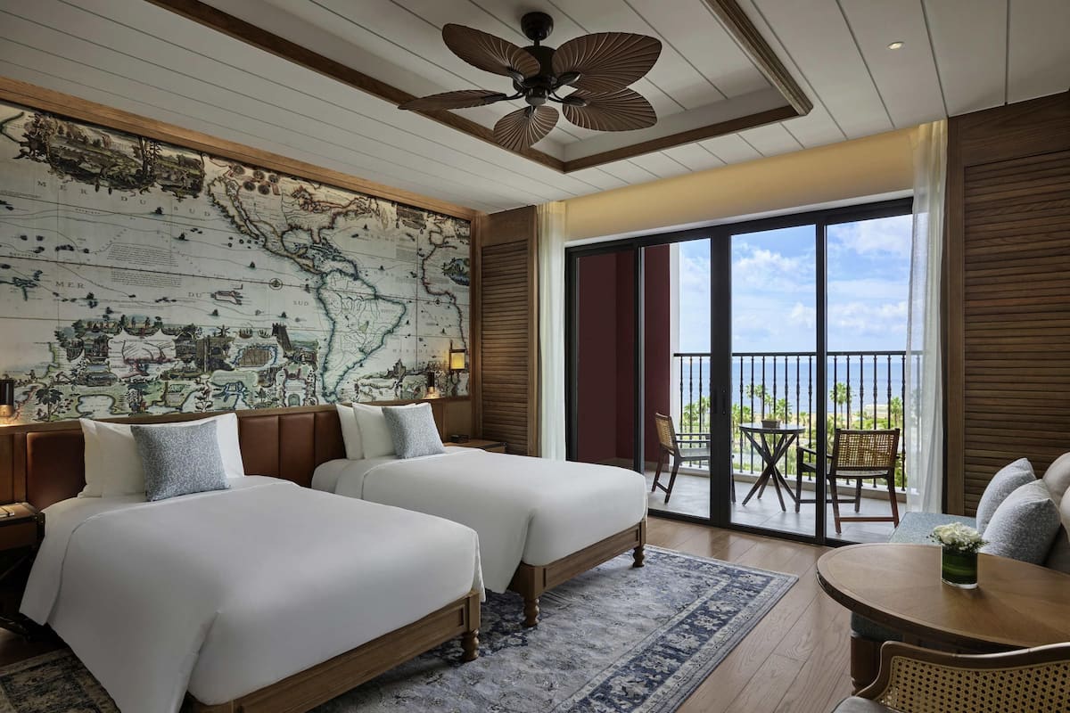 Habitación de hotel con dos camas, un mapa grande en la pared, un balcón con vistas y una zona de comedor.