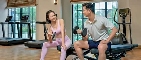 A gym with exercise equipment, large windows, and wooden floors.