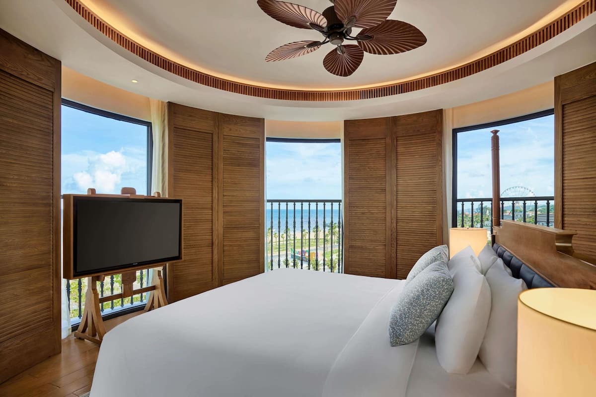 Una habitación de hotel moderna con una cama grande, un televisor y un balcón con vistas al mar.