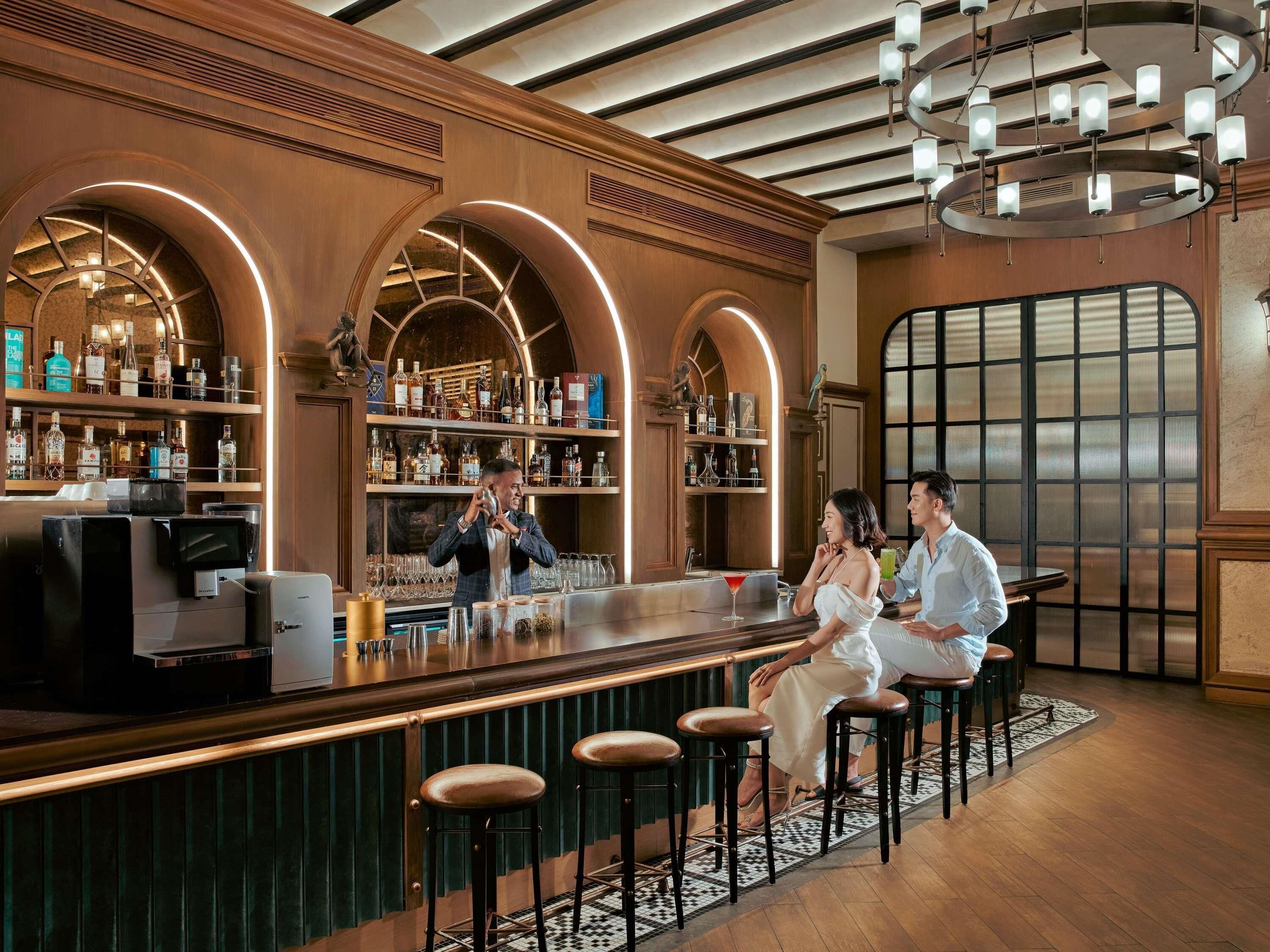 A bar area with a bartender, a couple seated, and shelves of liquor bottles.