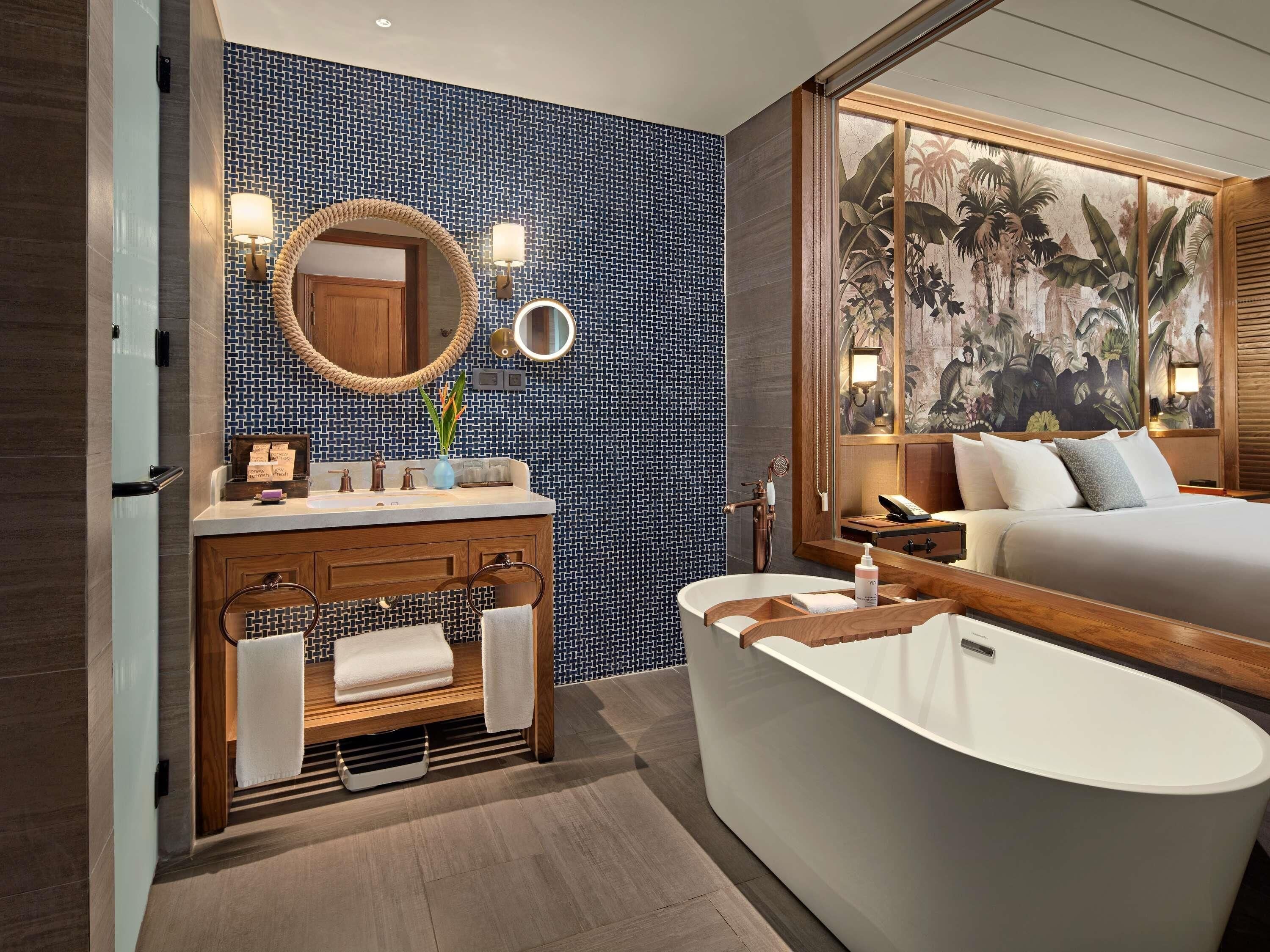 A modern bathroom with a freestanding bathtub, a vanity with a mirror, and a large window with a tropical mural.