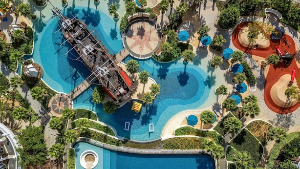 Vista aérea de un resort con varias piscinas, palmeras y una piscina central amplia.
