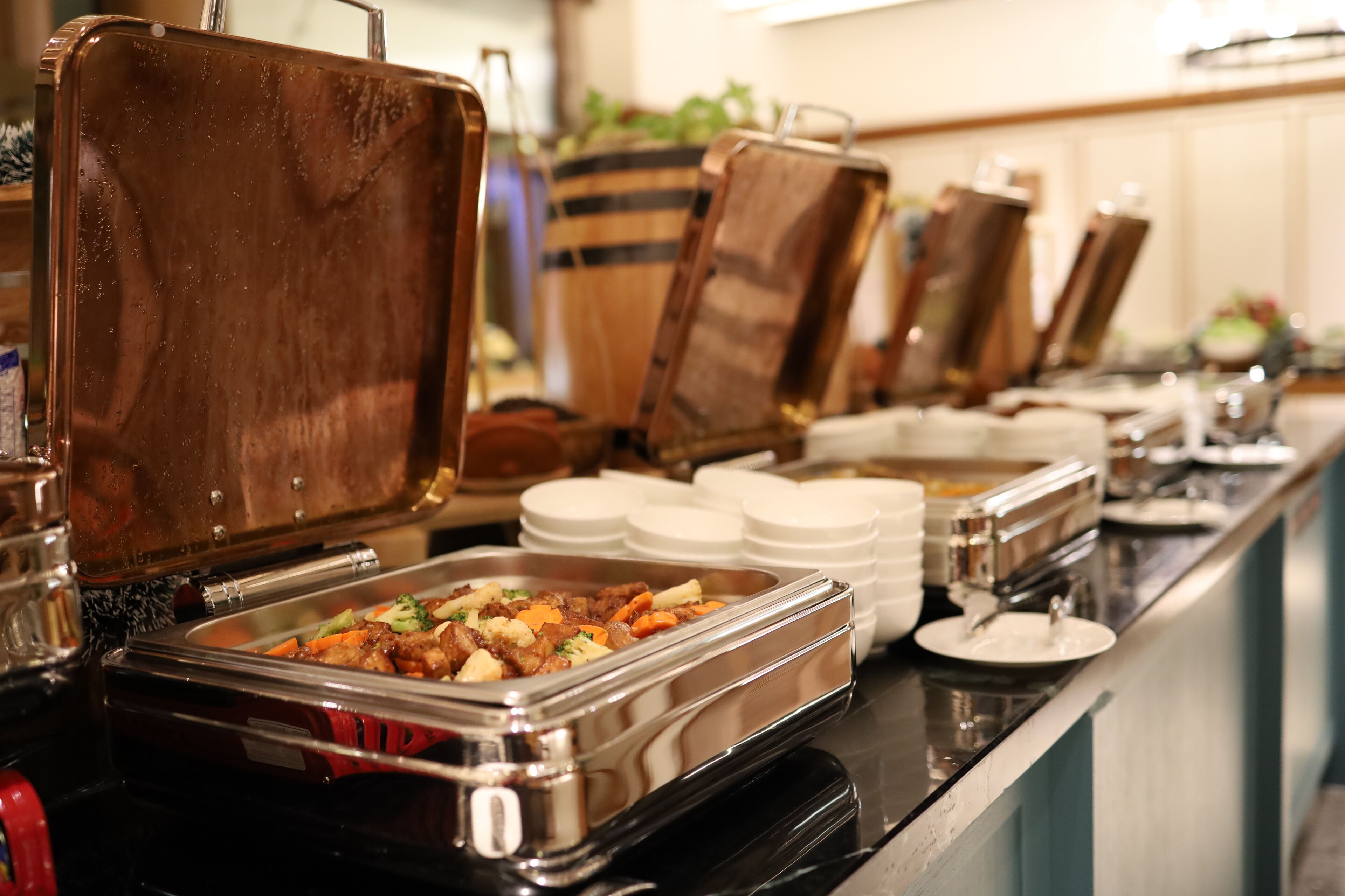 A buffet setup with multiple food stations, each with a covered serving tray and stacked white plates.