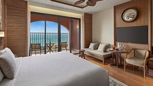 Habitación de hotel con una cama grande, un balcón con vistas al mar, un ventilador de techo y un televisor de pantalla plana.