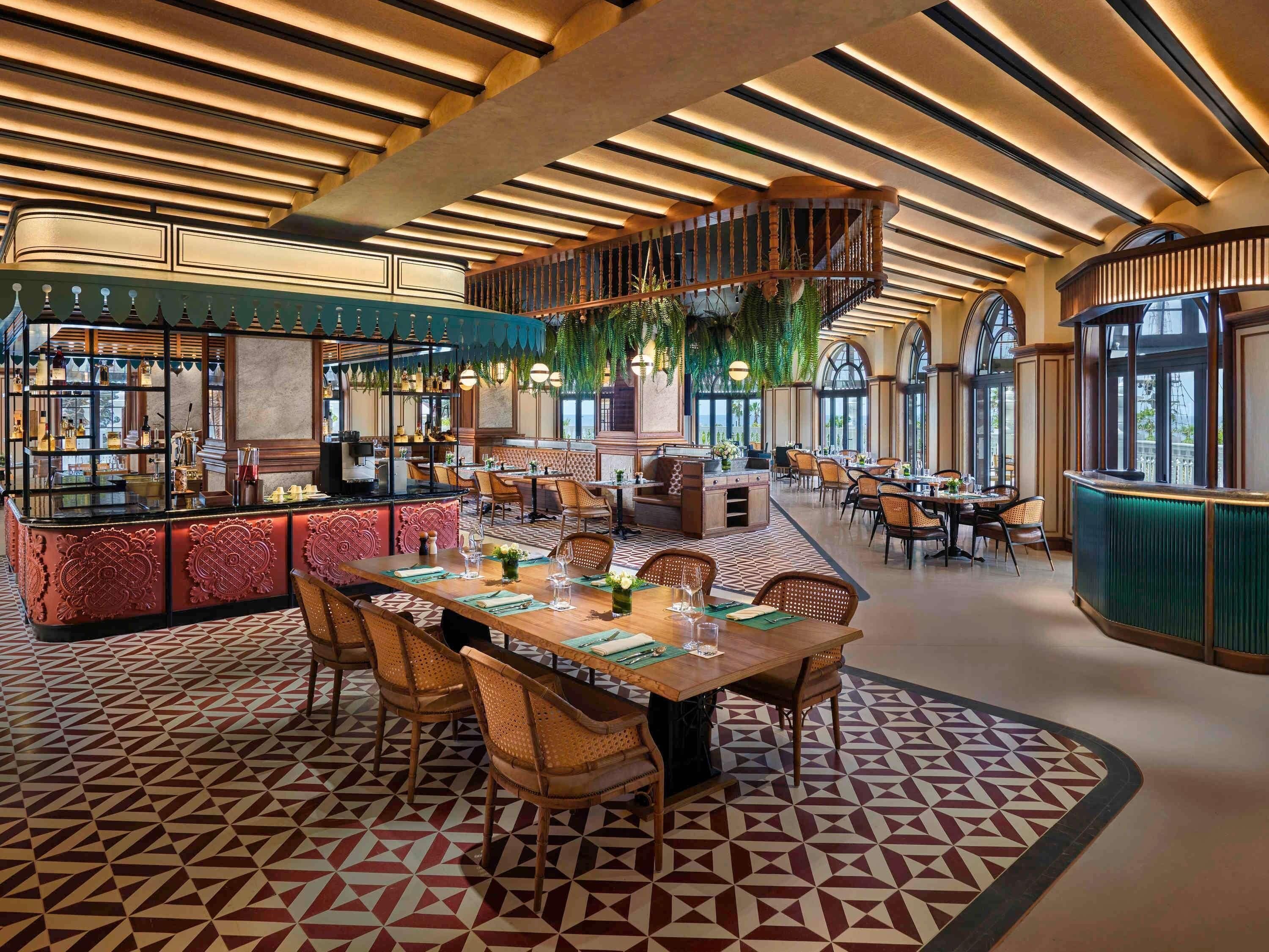 A restaurant with a geometric patterned floor, a central dining area with tables and chairs, and a bar area with a counter and shelves.
