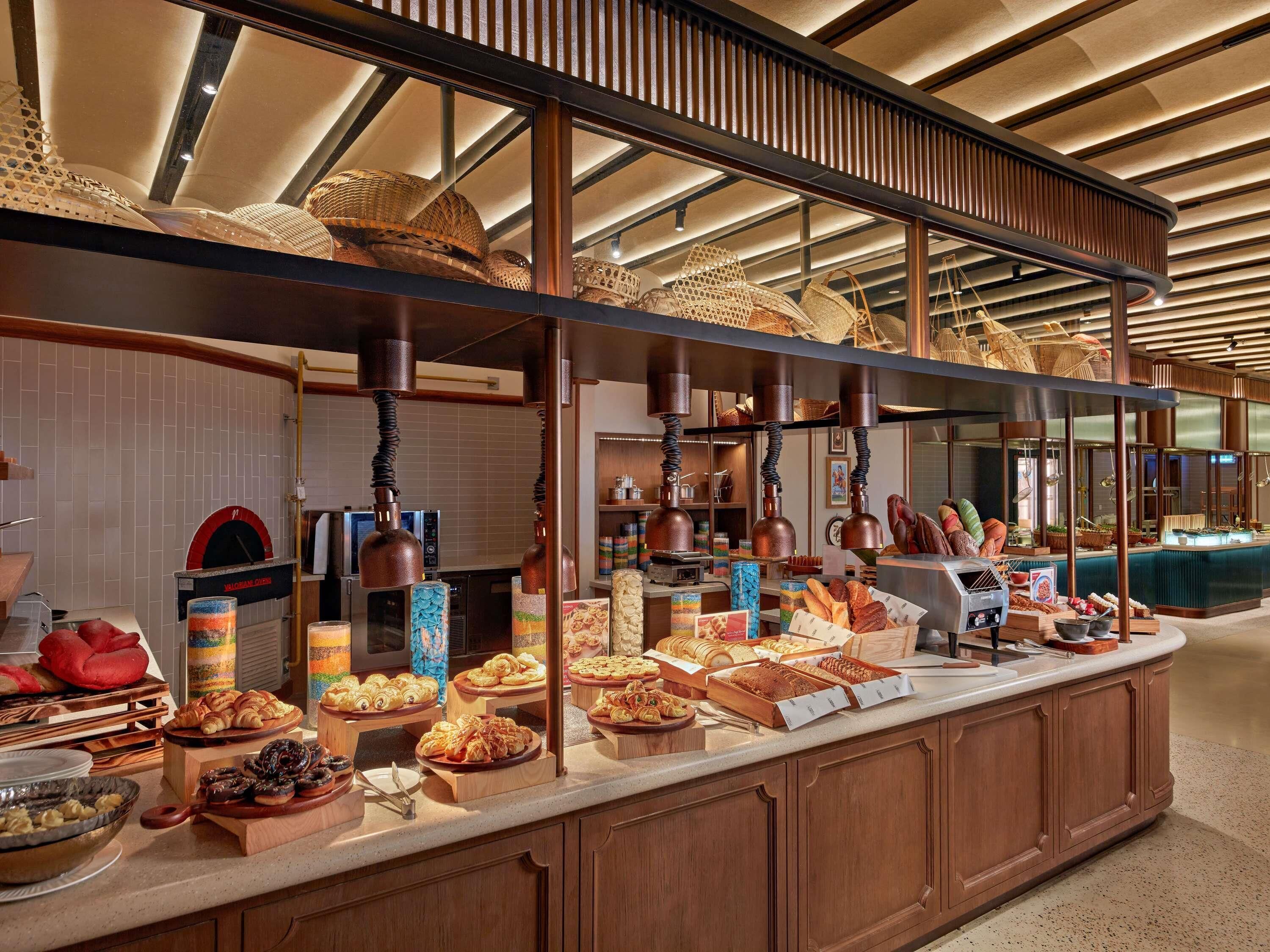 A buffet with various baked goods and pastries, a pizza oven, and a counter with a cash register.
