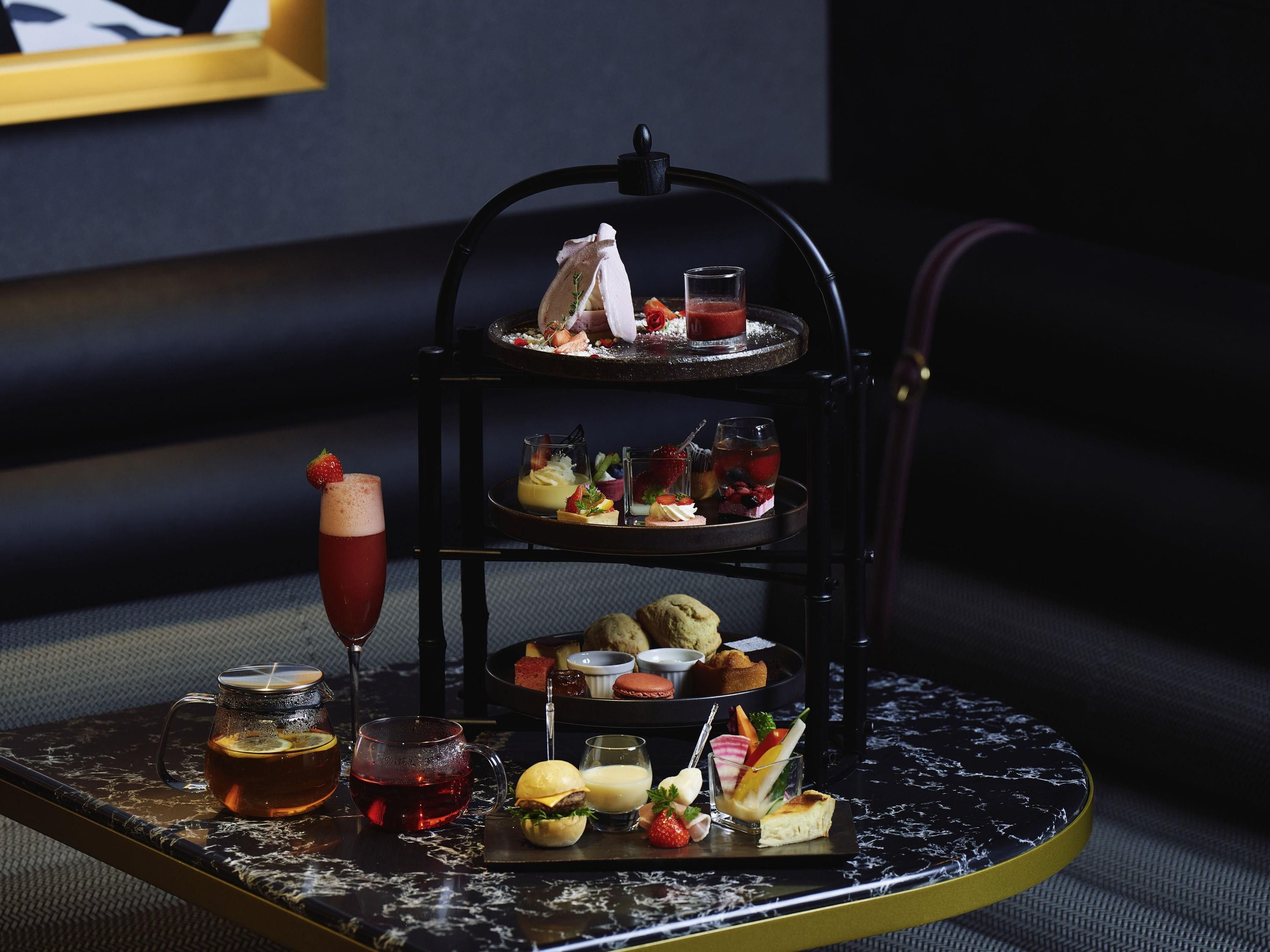 Ein mehrstufiger Dessertständer mit verschiedenen Süßigkeiten und Getränken auf einer Marmortafel.