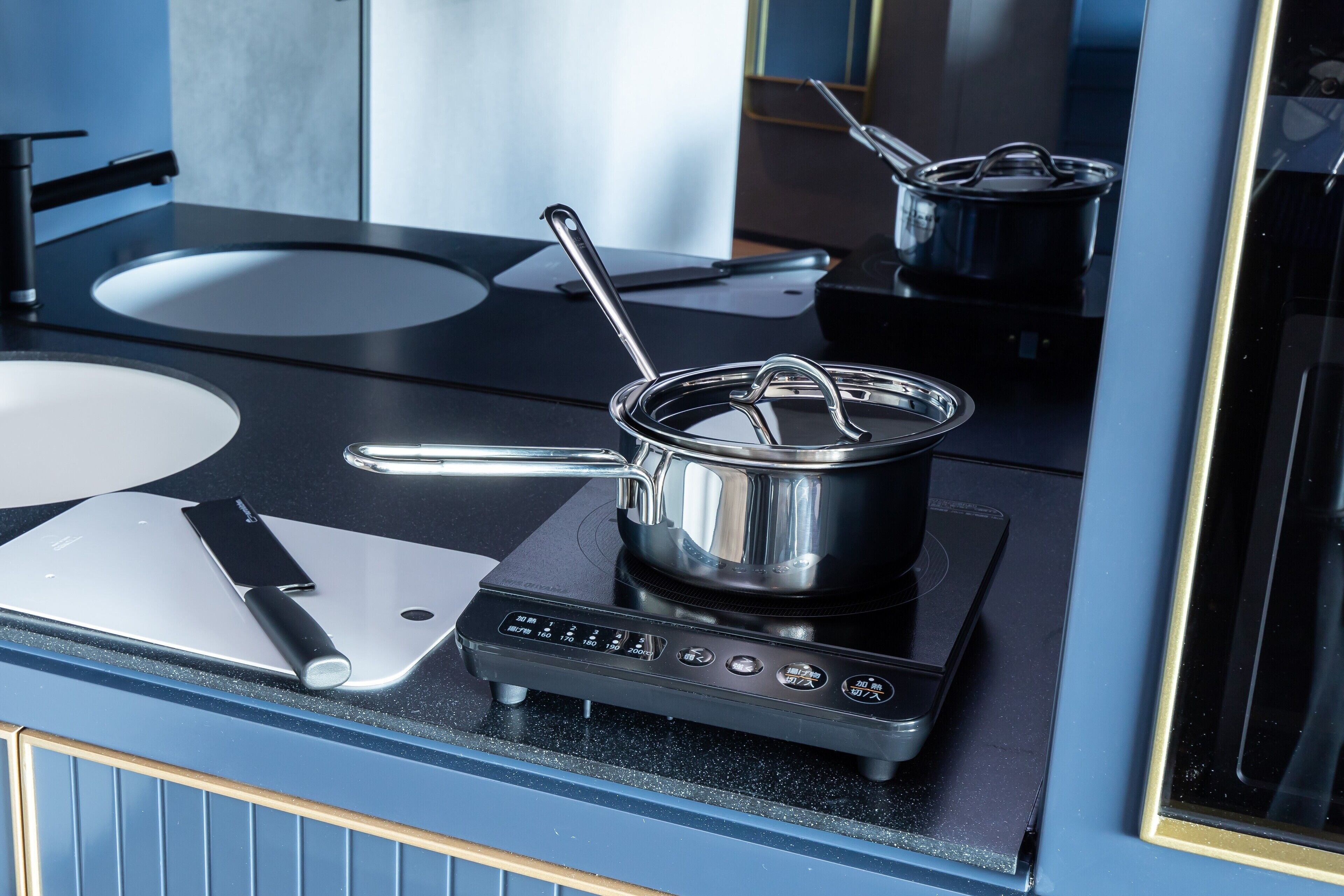 A modern kitchen with a black stovetop, a pot on the burner, and a cutting board with a knife.