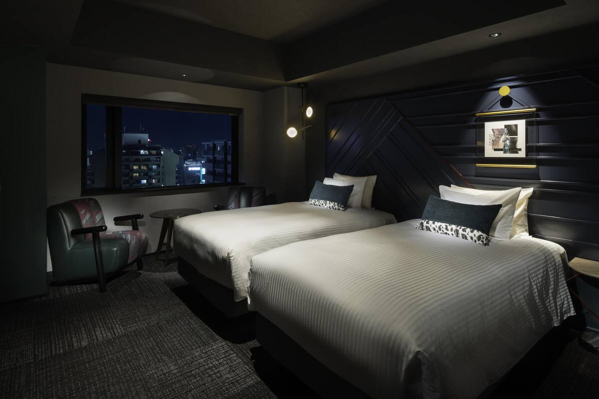 A hotel room with two beds, a desk, a chair, a city view, and a modern ceiling design.