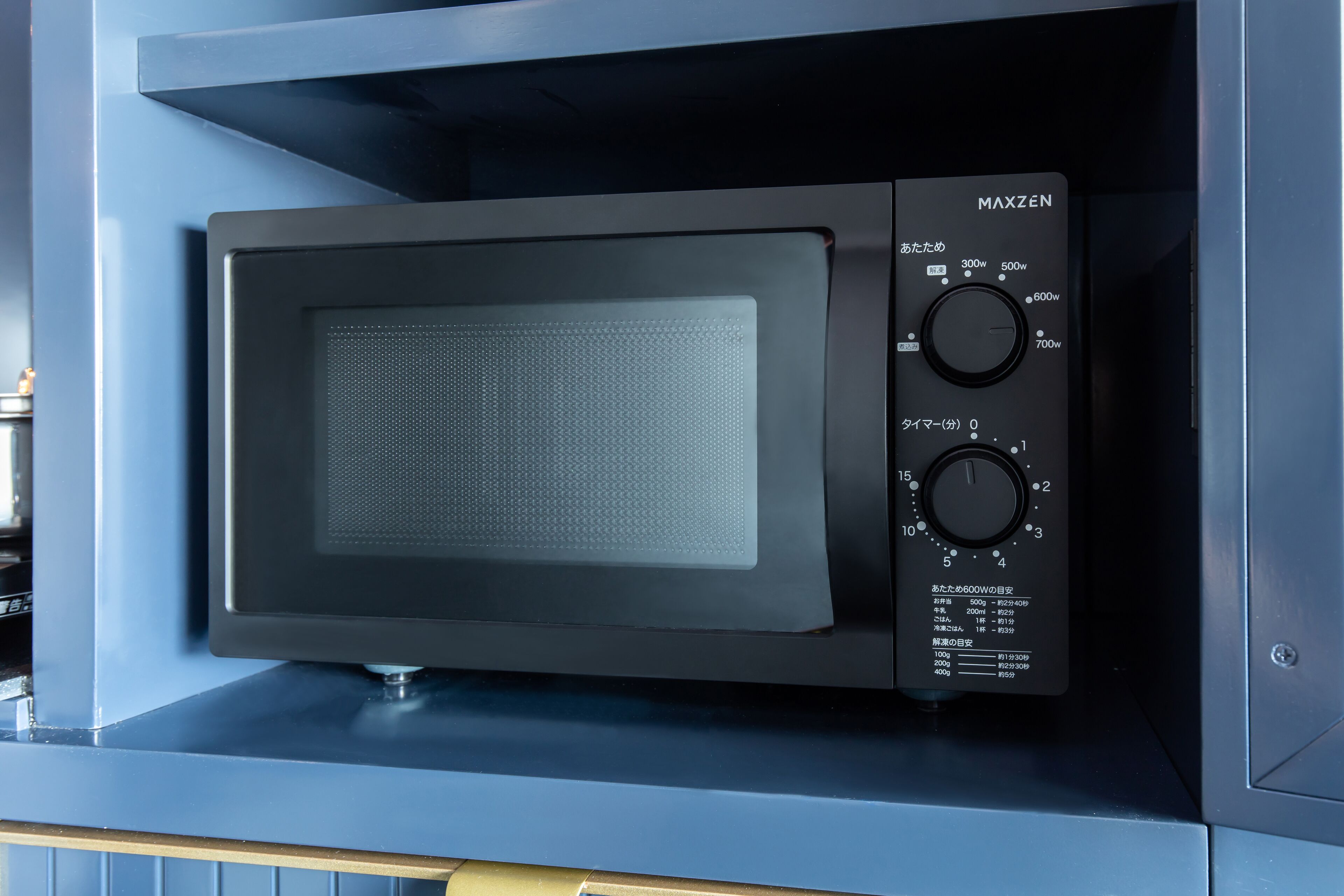 A black microwave with a digital display and control panel, placed inside a blue cabinet.