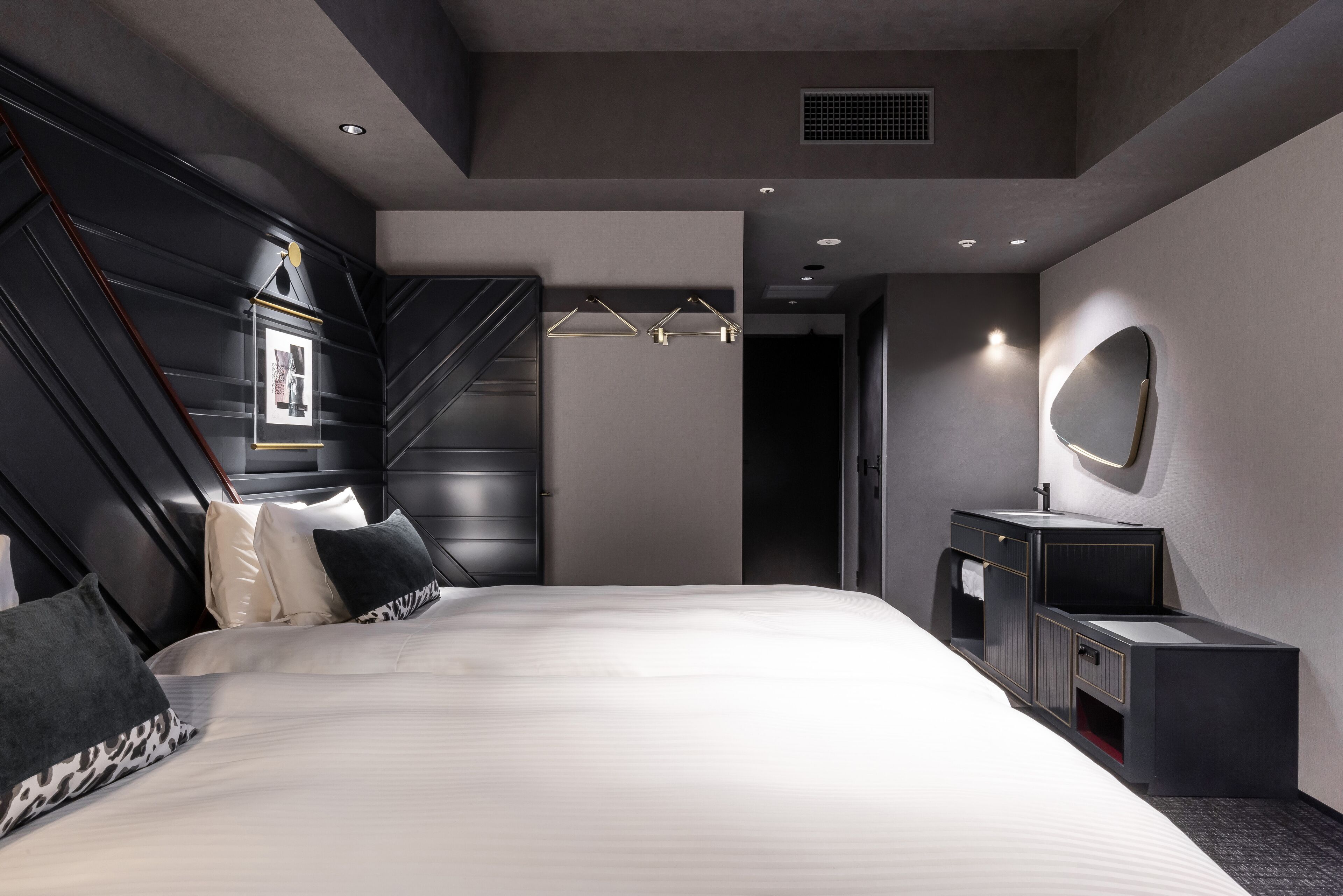 Una habitación de hotel moderna con una cama grande, un tocador con espejo y un diseño de pared original.