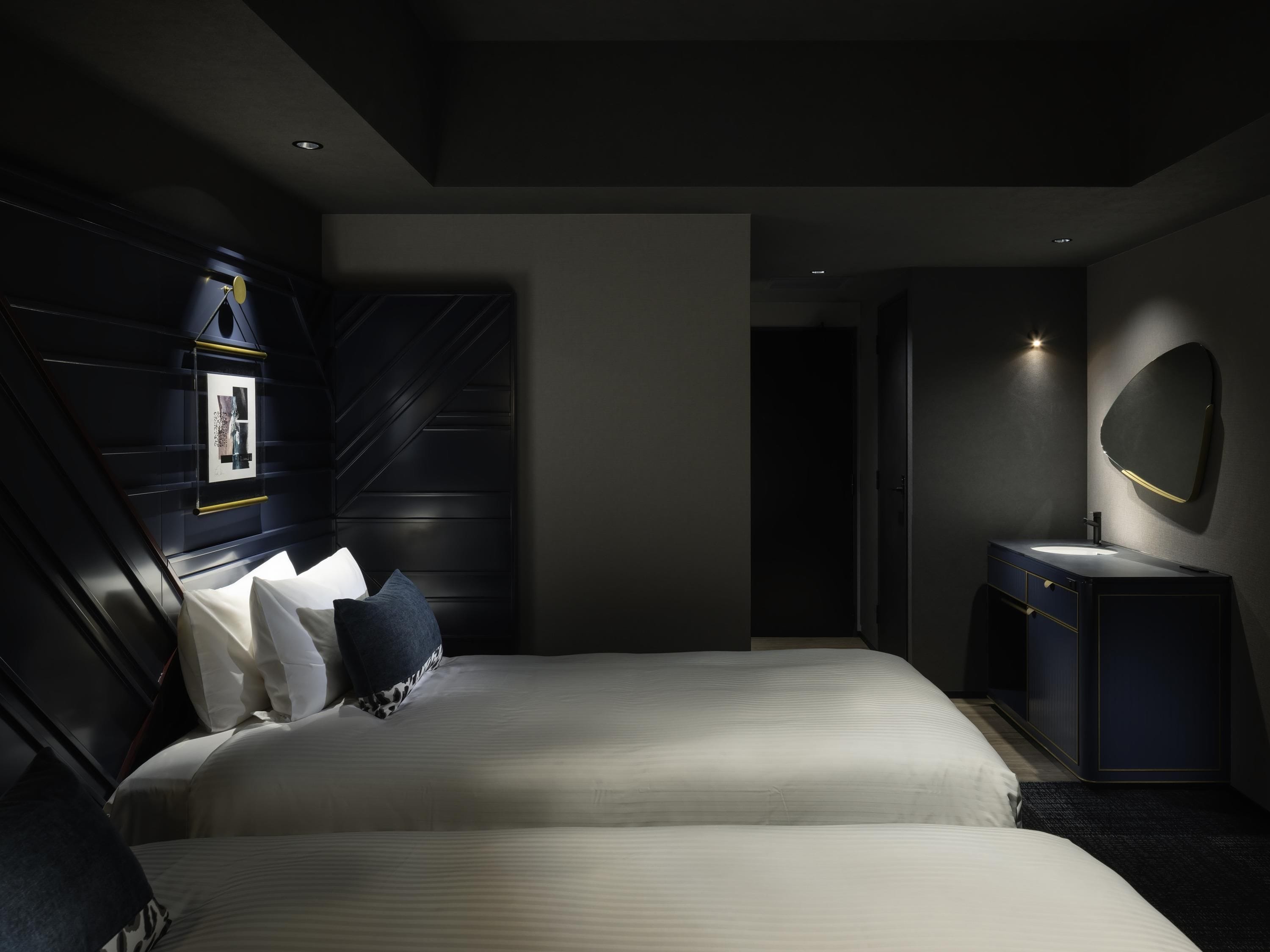 A modern hotel room with a large bed, a bedside table, a mirror, and a dark-colored wardrobe.