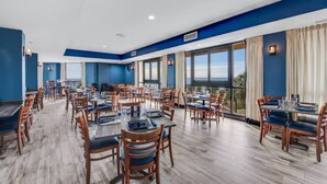A spacious dining area with multiple tables and chairs, large windows offering views of the outdoors, and a modern interior design with blue and white color scheme. - Best Layout/Relaxing OceanfrontSuite (Myrtle Beach)