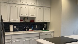 Una cucina con mobili bianchi, uno schienale nero e un piano di lavoro bianco.