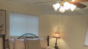 Una camera da letto con un letto, una ventola a soffitto, una lampada da comodino e una finestra con persiane.