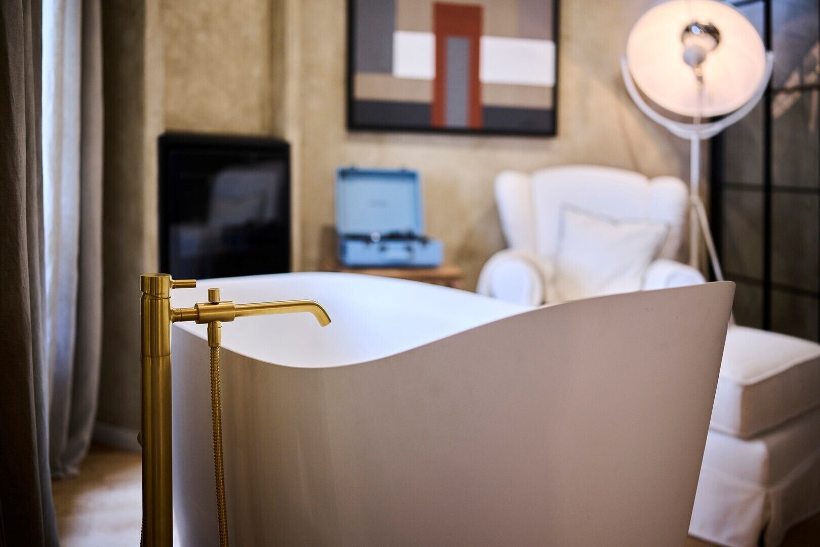 A modern bathroom with a gold faucet, a white bathtub, and a white chair.