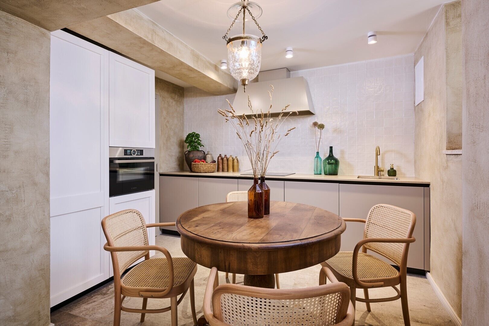 A modern kitchen with white cabinets, a round wooden table, and wicker chairs.