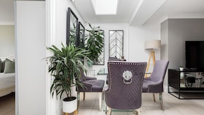 Una sala de estar moderna con comedor, que incluye un sofá, dos sillones, una planta en maceta, un televisor y una lámpara.