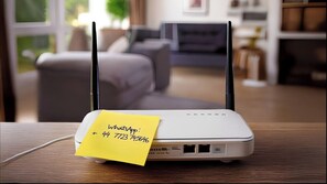Un router con una nota adhesiva amarilla pegada, sobre una mesa de madera en una sala de estar.