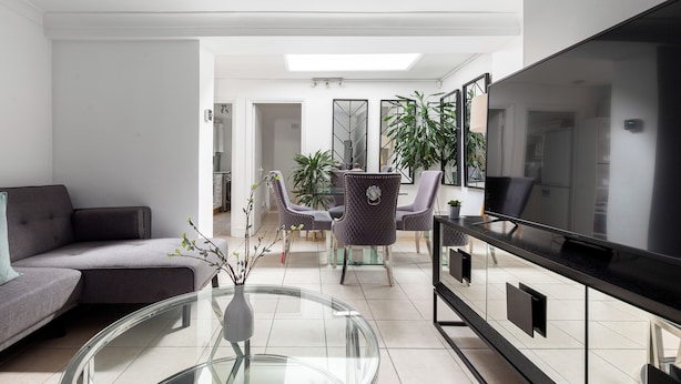 Una sala de estar moderna con sofá, una mesa de centro de vidrio, televisor y un comedor con sillas y mesa.
