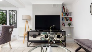 Una sala moderna con un televisor de pantalla plana, una estantería, una mesa de centro de cristal con un jarrón y una zona de estar confortable.